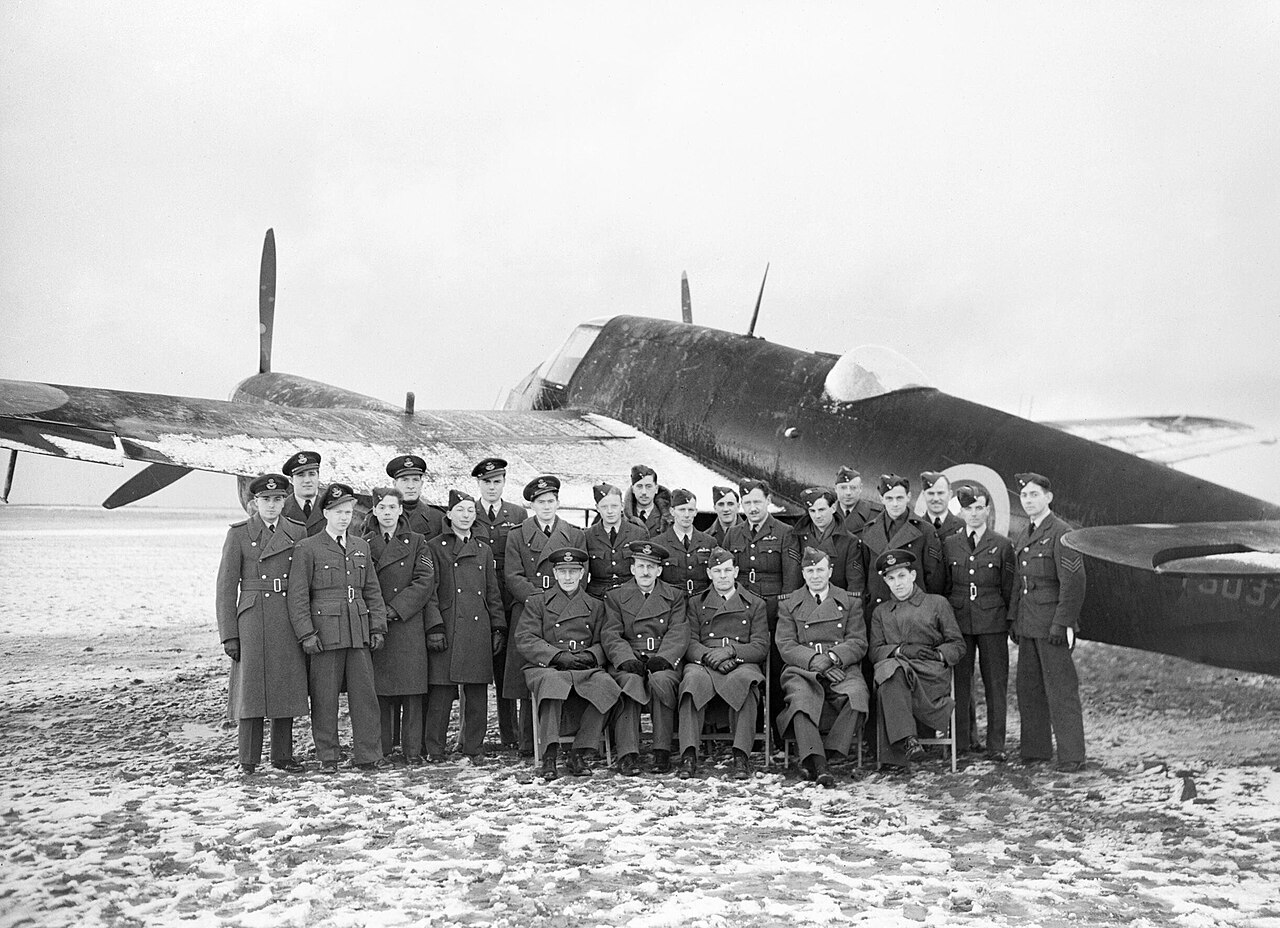 Personnel of 'B' Flight, No. 409 Squadron RCAF, pose for a formal portrait with one of their Beaufighter Mk IIs at Acklington, January 1942.
'B' Flight of No 409 Squadron, Fighter Command's first Canadian night-fighter unit, pose for a formal portrait with one of their Merlin-engined Beaufighter IIs Acklington, January 1942.