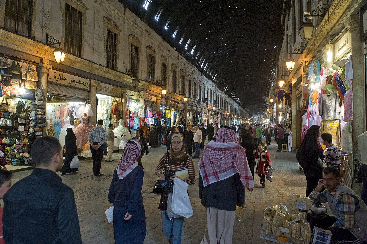 One of a set of pictures of this grand souq, some of its general appearance, some of architectural elements, some of the goods on sale. 
This سوق الحميدية is a bazar street that is special because it is on a grand scale, it has a grander aspect than the other suqs, which have longer histories, are more intimate. It was built under the Ottoman Sultan Abd al-Hamid II (1876-1909), following a former Roman axis, that probably connected to the western side of the temple of Jupiter, where we now find the Umayyad Mosque. That roman area had deteriorated. The originally wooden roof of the suq has been replaced in 1912 by a metal one.