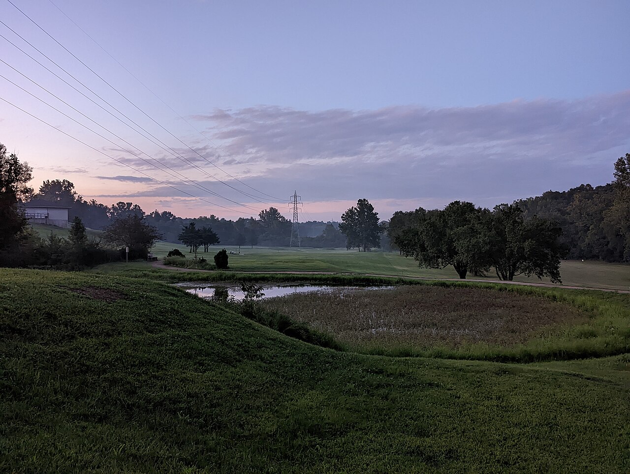 This is a photo taken on September 3, 2022, on the ground in Pomme Creek Park in the city of Arnold, Missouri, in the United States. The camera is facing north (towards St. Louis) at sunset with a haze on the horizon.
