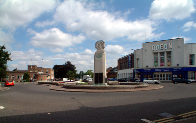 Beckenham War Memorial. This memorial commemorates the men and women of Beckenham who lost their lives in two World Wars. It was unveiled on Sunday 24th July 1921. The memorial was designed by Mr. Newbury A. Trent, R.B.S., is approximately 7.5 metres high, and is a rectangular white Portland stone column.
This view is from the south, with the High Street to the right. On the left is the post office.