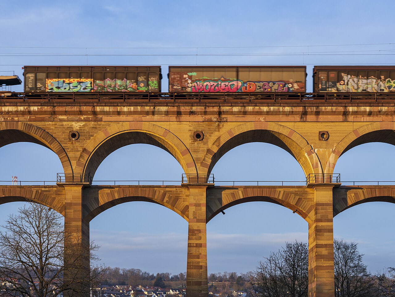 Bietigheim-Bissingen, Germany: view of the central part of the Bietigheim Viaduct with a passing goods train and the view of the downtown of Bietigheim. Photo taken at a winter’s evening with evening sun.