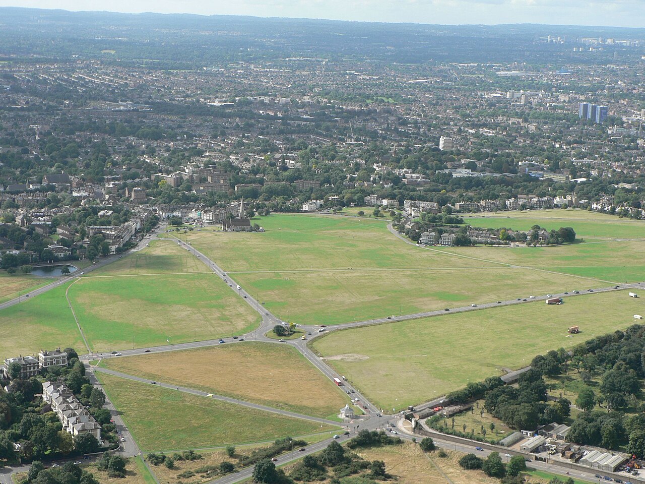 An aerial view of the Heath at Blackheath, London. A minor ridge after a short dip reaching a peak at Shooter's Hill in the east; here the towers of central Lewisham and Croydon are beyond to the south-west (right). The backdrop is the long crest of the North Downs in the far south of Bromley and adjoining Surrey