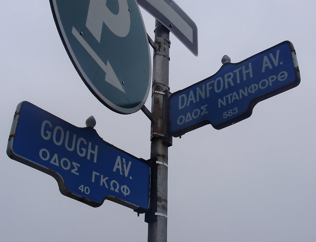 Bilingual English/Greek street signs for Danforth Avenue and Gough Avenue in Toronto's Greektown neighborhood.
