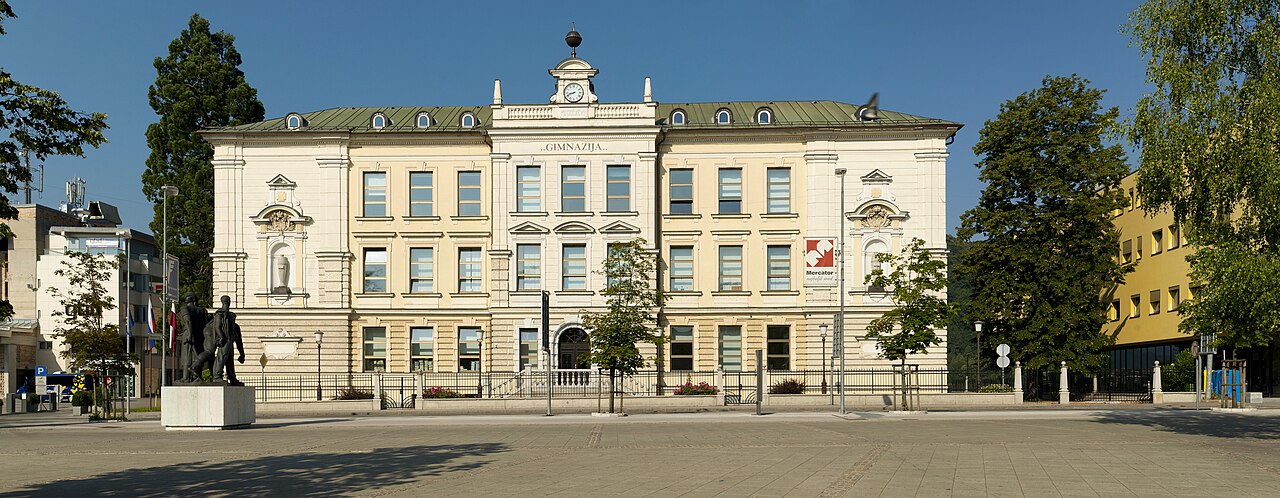 Kranj Gymnasium, next to Slovene Square (Slovenski trg). The historicist building was completed in 1897 according to plans by Viljem Treo (1845–1926) from Ljubljana. The sculpture in the front is work by Lojze Dolinar (1893–1970).