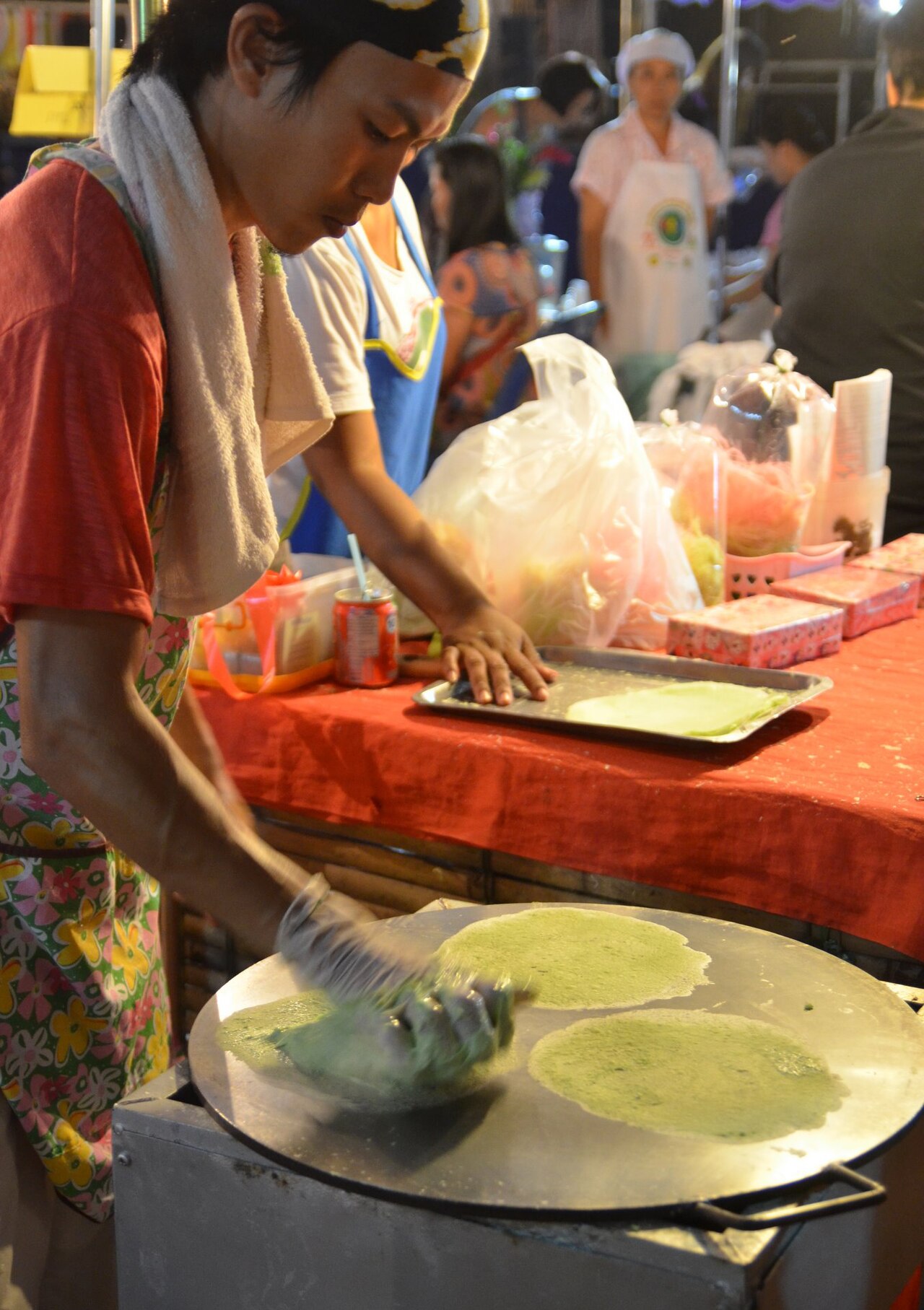 Making roti sai mai (Thai script: โรตีสายไหม). It literally means "silk roti" (roti is a flat bread of Indian origin). These ultra thin pancakes are made by rubbing a sticky dough on to a hot plate. They are used as a wrap for a kind of candy floss. This photo was made at a night market in Uttaradit, Thailand. The final result can be seen here.