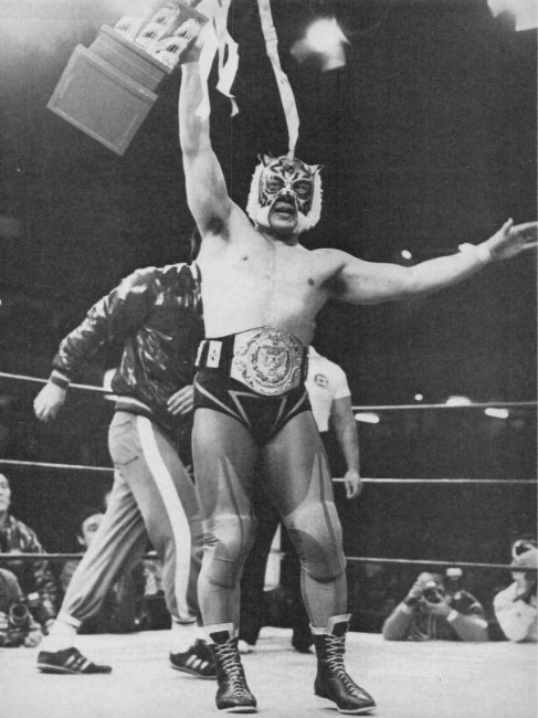 Tiger Mask portant la ceinture de champion poids lourd junior de la World Wrestling Federation ainsi qu'un trophée célébrant sa victoire.