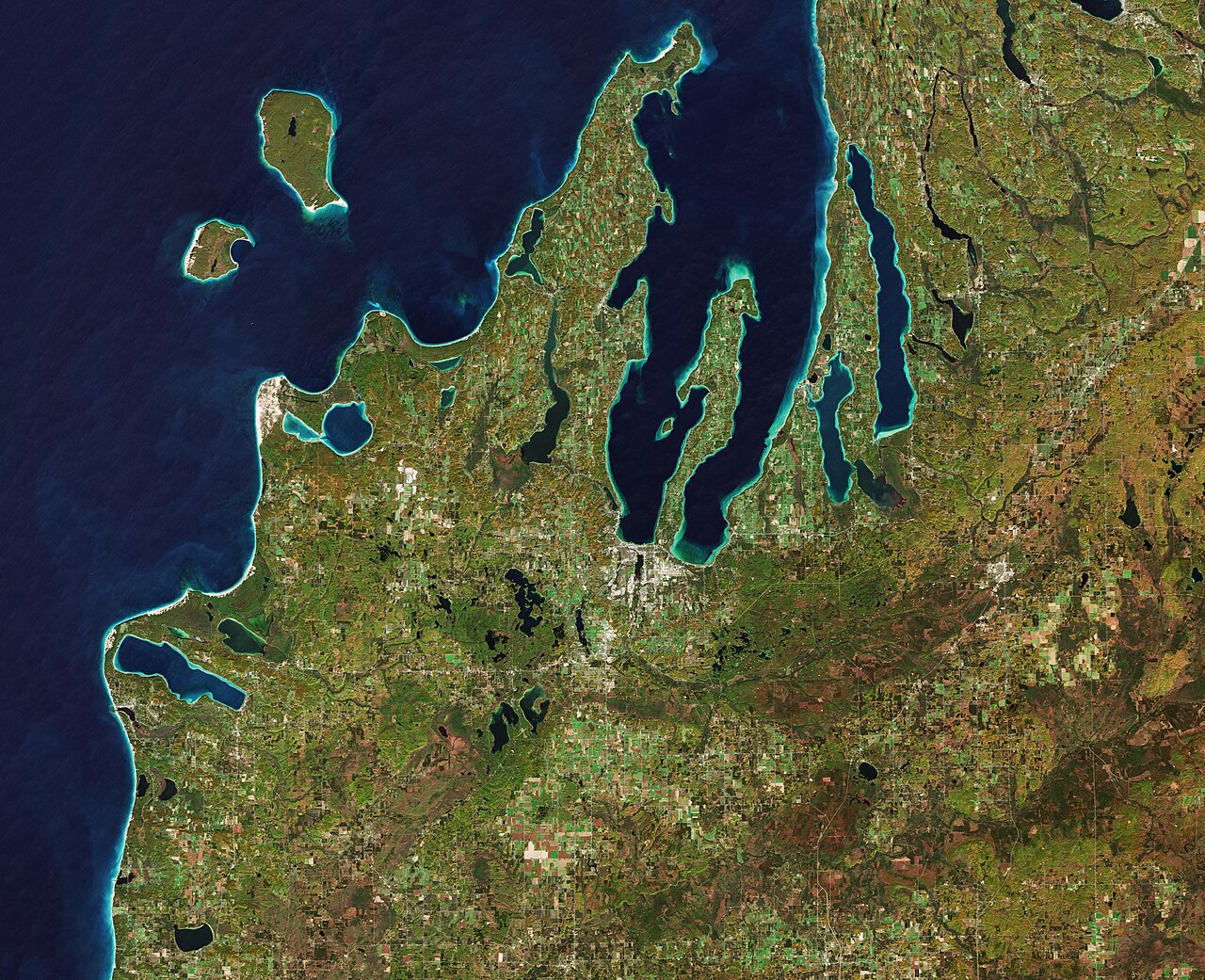 The Copernicus Sentinel-2 mission takes us over the Leelanau Peninsula on the northwest coast of Northern Michigan, US.The region is shaped by rolling hills, large inland lakes shaped by glaciers around 20 000 years ago which form the basis for great farmland. The body of water that surrounds the peninsula is Lake Michigan, one of the five Great Lakes of North America and the only one located entirely within the US.In the image, the bright turquoise in the water shows sediments, algae and chlorophyll in the shallower waters along the shore. The greener colours visible in Lake Leelanau to the north, Platte Lake to the west, and several inland bodies of water are due to a combination of a high chlorophyll and plant content.The Sleeping Bear Dunes Lakeshore extend for around 55 km along the coast of the peninsula, and is visible in light brown. The name comes from an Ojibwa legend in which a mother bear and her two cubs swim across the lake trying to escape a forest fire. The two cubs are said to have disappeared in the process, and the mother bear waited for weeks for them to re-surface before finally falling asleep and never waking. Touched by her suffering, a powerful spirit is said to have covered her with sand, and raised the two cubs above the water, creating the North and South Manitou islands, visible north of the peninsula.A more realistic explanation of the creation of the Sleeping Bear Dunes is geology. During the last Ice Age, glaciers spread southwards from Canada burying this area under sheets of ice. During the process, piles of sand and rock were deposited in the area. When the ice retreated and melted, it left the hilly terrain that exists along the lake today. The area is popular for hiking and climbing.This image, which was captured on 18 October 2018, is also featured on the Earth from Space video programme.