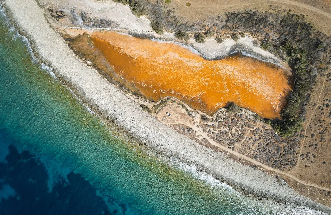 Downward view of orange coastal salt pond, Agios Stefanos, Mykonos, Greece