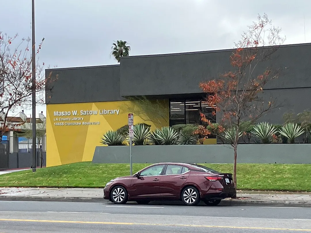 Masao W. Satow Library: A brick structure with a yellow wall indicating the entry; a car is parked on the street in front.