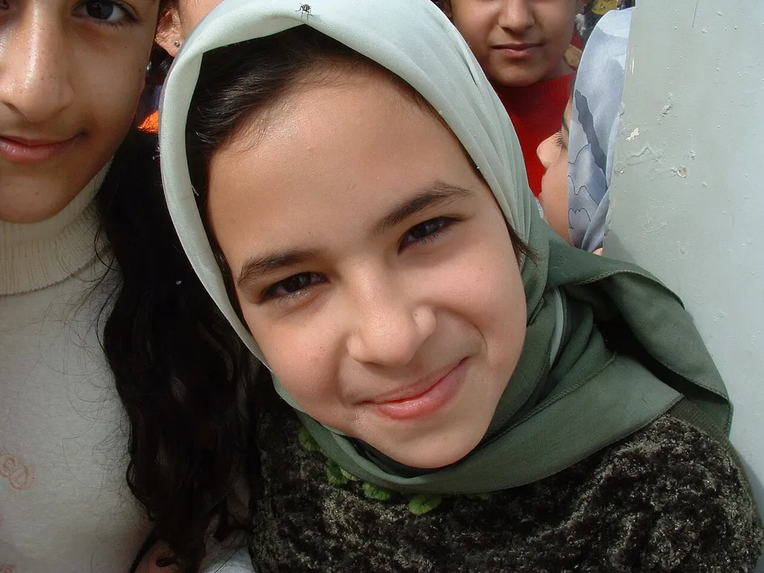 Iraqi girl smiles. Iraqi girl living next to Al Daura Oil Refinery in Baghdad pauses for a smile amongst jostling children. I managed to snap a picture of this stunning looking Iraqi girl while I was touring Al Daura Oil Refinery as part of the Human Shield Action to Iraq. I took this photo, and many more, of the children living next to the refinery where their parents worked. They were all quite enjoying themselves and I managed to get mobbed a couple of times. I often look back on this photo and wonder if she, and her friends, are still alive. I hope to go back one day and find out. —Christiaan 11:58, 5 Feb 2005 (UTC)
