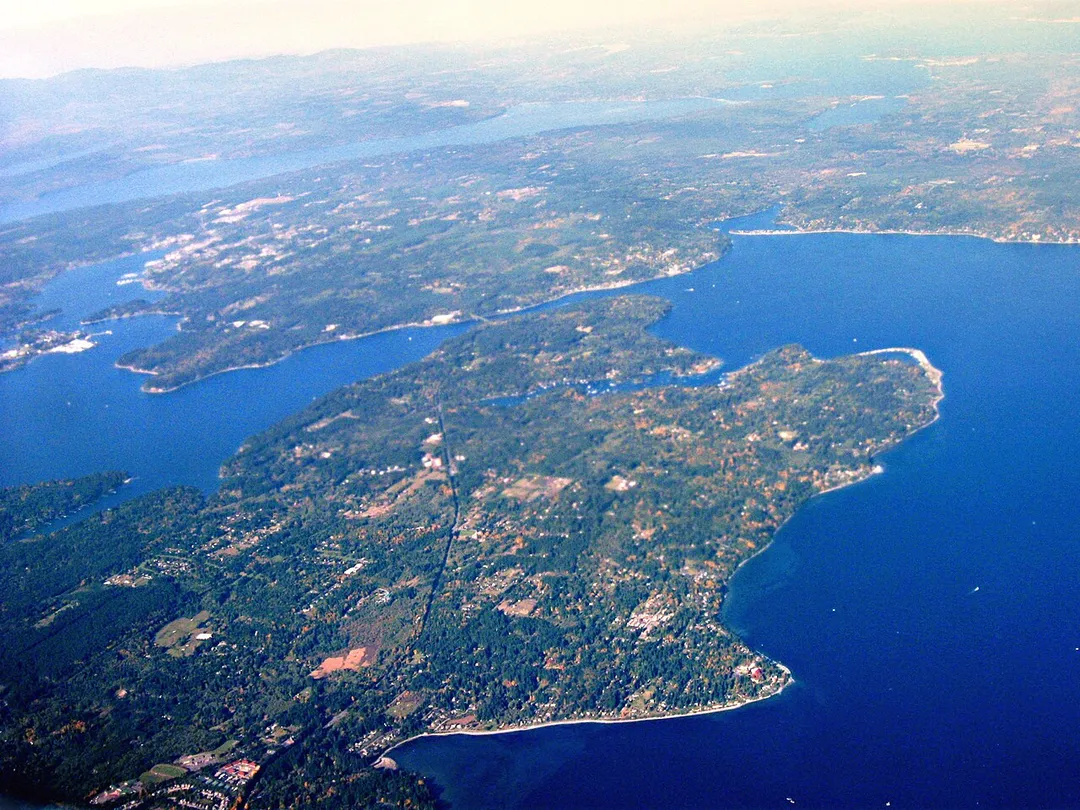 Aerial view of Bainbridge Island (bottom center/left) and Agate Passage (center), facing north north west. Beyond Bainbridge Island is Port Orchard Bay (left center) and the Olympic Peninsula (top). Taken by myself from a commercial airliner window.