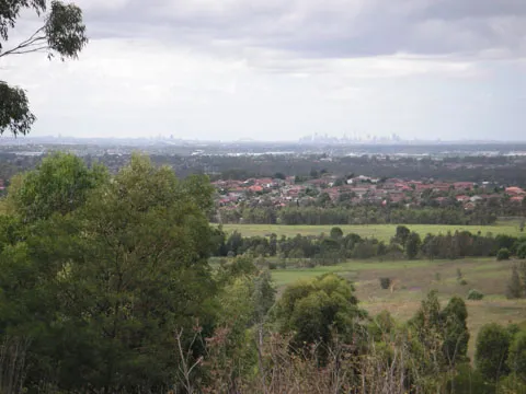 View of the city of Sydney taken from the lookout in Western Sydney Regional Park. The Sydney Harbour Bridge can be viewed in the middle of the horizon with the main city area to the right and North Sydney to the left. The suburb in the foreground is Bossley Park.