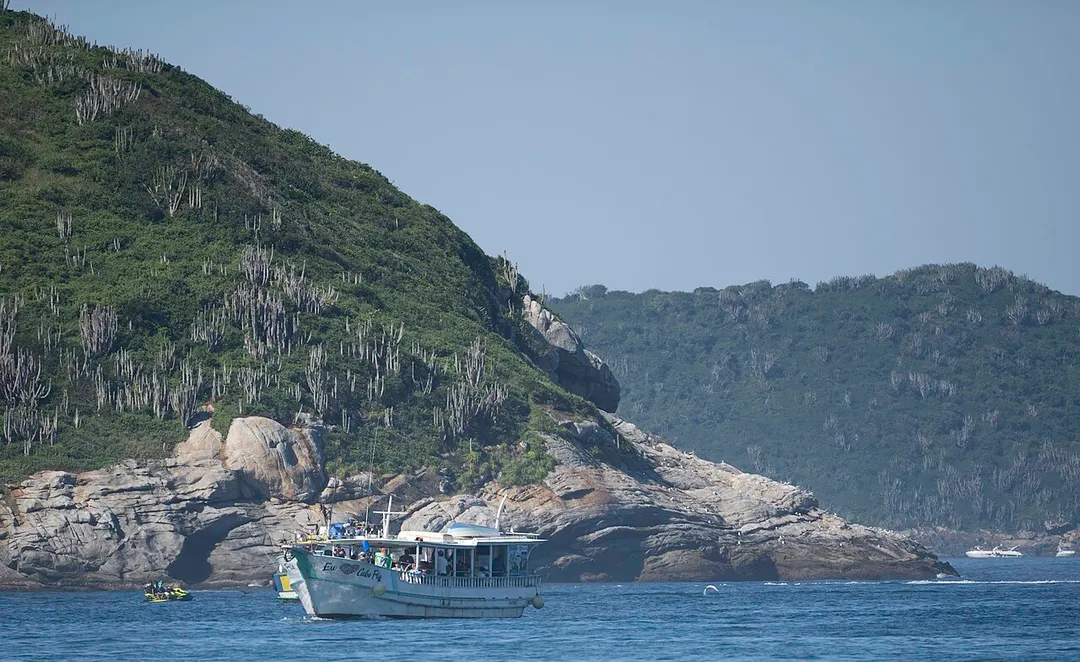 Tour boat Eu Amo Cabo Frio near cactus-covered coastal hills in Cabo Frio, Rio de Janeiro state, Brazil.