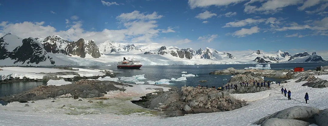 Panorama - penguin colonies, cruise ship & tourists, Petermann Island (foreground), Kiev Peninsula of Antarctic Peninsula (background).