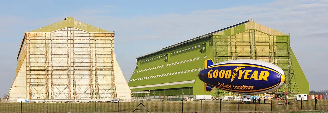 Goodyear Blimp 'Spirit of Safety I' (G-HLEL) moored at Cardington Airship Sheds, Bedfordshire, UK. A grey semi-trailer (articulated lorry) can be seen under the tail. It was parked just in front of the building, Shed 2, and gives some idea of the sheer scale of the building.