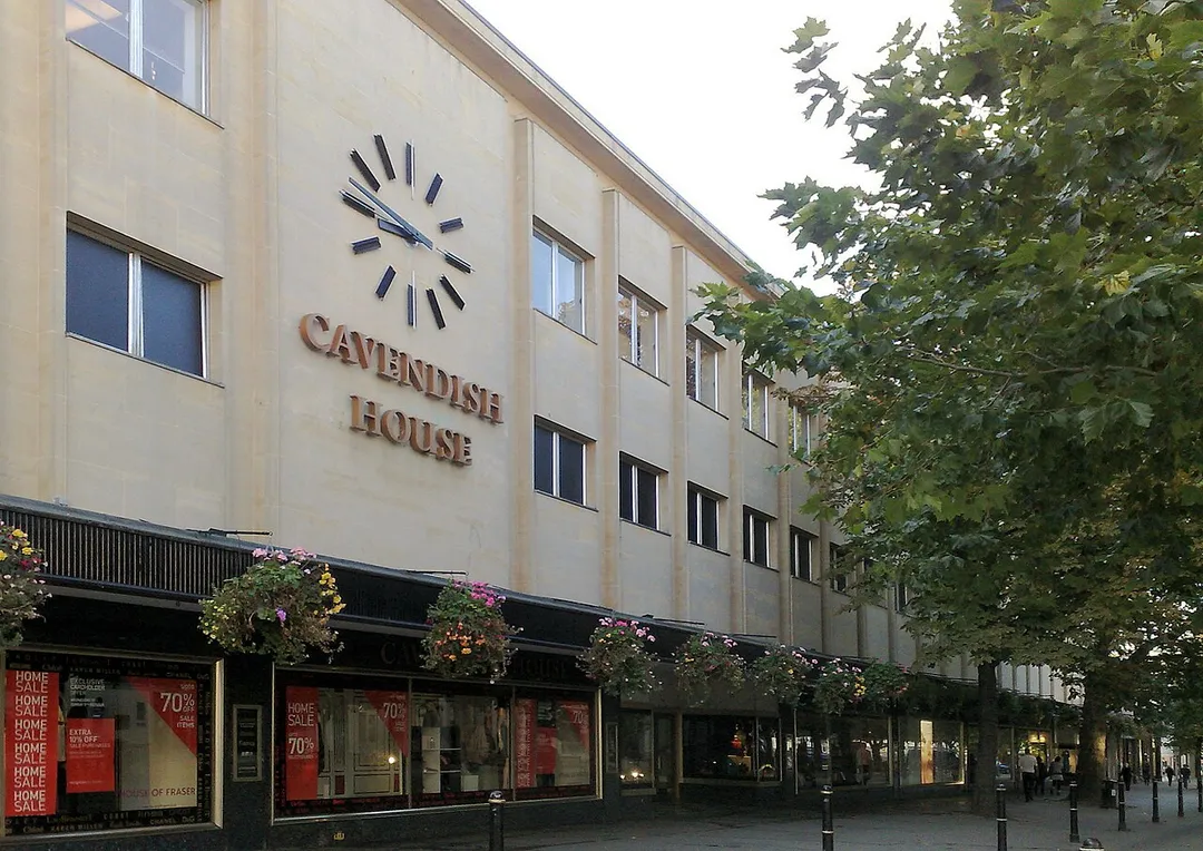 October 2008 photo of Cavendish House department store in Cheltenham, main Promenade entrance, side-angled shot showing most of the 287-foot frontage and clock as per 1931 refurbishment onwards. Also shows flower baskets and bollards on pedestrian area of the Promenade.