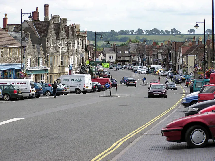 The wide main street of Chipping Sodbury. Cars are parked where market stalls would once have been.   
Taken by Adrian Pingstone in July 2004 and released to the public domain.