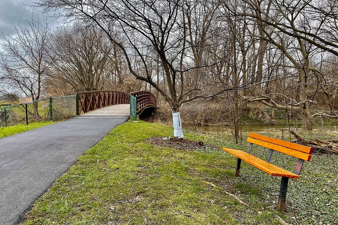 The Judith S. Chick Memorial Bridge carries cyclists and pedestrians over Ellicott Creek near the east end of the Ellicott Creek Trailway in Amherst, New York. Chick (1942-2015) made a name for herself in the wake of a disastrous flood in February 1985 as founder of Concerned Citizens for Ellicott Creek Flood Control, an effort that culminated in a trip to Washington, D.C. to personally urge Congress to pass the namesake legislation. The completion of the project in 1988 opened the doors to the construction of the 4.4-mile original portion of the Trailway, which extends in a northwesterly direction roughly parallel to Ellicott Creek (hence its name) from Ellicott Creek Trailway Park on North Forest Road, passing through the North Campus of the University at Buffalo and the sprawling Audubon Industrial Park before ending at Ellicott Creek Park in nearby Tonawanda. A southward extension of the path, leading to the Audubon Recreation Complex on Amherst Manor Road, added 2.2 miles to the total length when it opened in May 2000.