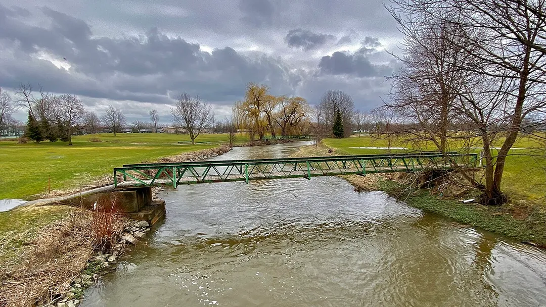 A view southward along Ellicott Creek from the Judith S. Chick Memorial Bridge near the east end of the Ellicott Creek Trailway in Amherst, New York. Chick (1942-2015) made a name for herself in the wake of a disastrous flood in February 1985 as founder of Concerned Citizens for Ellicott Creek Flood Control, an effort that culminated in a trip to Washington, D.C. to personally urge Congress to pass the namesake legislation. The completion of the project in 1988 opened the doors to the construction of the 4.4-mile original portion of the Trailway, which extends in a northwesterly direction roughly parallel to Ellicott Creek (hence its name) from Ellicott Creek Trailway Park on North Forest Road, passing through the North Campus of the University at Buffalo and the sprawling Audubon Industrial Park before ending at Ellicott Creek Park in nearby Tonawanda. A southward extension of the path, leading to the Audubon Recreation Complex on Amherst Manor Road, added 2.2 miles to the total length when it opened in May 2000.