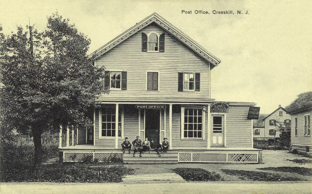 Matte black and white photo postcard of the Post Office, Cresskill, New Jersey. Back is divided and reads "No. B8034 Made in Germany" It is published by the American News Company, New York. Its logo on the back of a shamrock is surrounded by the word "EXCELSIOR" and underneath "Leipzig Dresden Berlin".  It bears a cancelled one-cent stamp of George Washington
