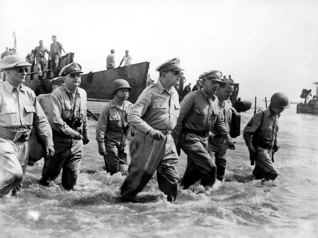 Douglas MacArthur wades ashore during initial landings at Leyte, Philippine Islands. Left to right: Philippine President Sergio Osmena; Lieutenant General George Kenney (obscured); Colonel Courtney Whitney; Brigadier General Carlos Romulo; General Douglas MacArthur; Lieutenant General Richard Sutherland; CBS radio correspondent Bill Dunn; Staff Sergeant Francisco Salveron