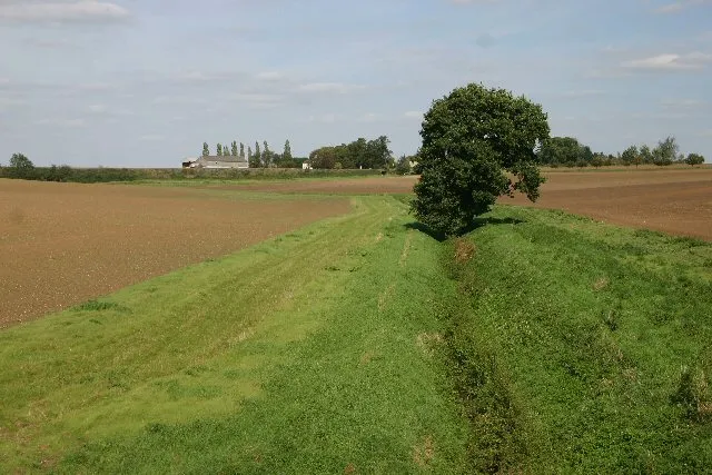 Stream at Elmswell. This stream divides the fields; in the distance is the railway line on an embankment and behind it, Elmswell Hall.