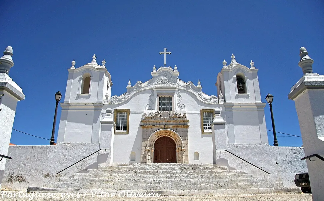 De remota fundação, a Igreja Matriz da bonita povoação de Estômbar, que integra o concelho da Lagoa, foi remodelada no reinado de D. Manuel I. No entanto, o século XVIII havia de a reformar quase totalmente, conservando este templo ainda alguns sinais de épocas anteriores. A Matriz de Estômbar é dedicada ao apóstolo S. Tiago e foi decretada em 1984 Monumento Nacional. Situada no Largo da Igreja desta povoação algarvia, a Matriz de S. Tiago de Estômbar ergue-se no topo de um morro, ao qual se acede por escadório de vários patamares.
Antecedida por um adro, a imponente frontaria revela a reforma da segunda metade do século XVIII. Na fachada rasga-se um belo portal quinhentista da época manuelina, em arco de volta perfeita, enquadrado por estrutura de pedra idêntica (grés escuro local); as suas colunas apresentam decoração naturalista e curiosos e invulgares motivos antropomórficos - músicos com os seus instrumentos e figuras femininas, talhados com alguma rudeza, mas imbuídos de uma rica sensibilidade popular.
A estrutura do portal é encimada por movimentadas aletas, sobre as quais se rasga uma janela retangular, ladeada por motivos barrocos curvilíneos. A porta é flanqueada por duas janelas retangulares gradeadas. A empena desenha linhas ondeadas, encimada por frontão curvo, pináculos e cruz latina, no tímpano do qual se inscreve um medalhão barroco ornamentado. A fachada é flanqueada por duas torres sineiras quadrangulares, marcadas por cunhais salientes e divididas em dois pisos. O superior é rasgado por ventanas, que apresentam cobertura curva marcada por várias urnas sobre pedestais.O interior é formado por três naves, repartidas em quatro tramos por arcos de volta perfeita, forrados por painéis de azulejos setecentistas. As paredes laterais das naves apresentam idêntico revestimento cerâmico.
Sobre o arco triunfal e circundando um óculo, expõe-se um painel cerâmico alusivo à Ascenção. A capela-mor é totalmente forrada com azulejos setecentistas (1719), figurando episódios hagiográficos e graciosos anjos brincando. O retábulo-mor é uma composição do barroco tardio, decorado com três faustosos medalhões e ostentando num dístico a data de 1760. In Infopédia [Em linha]. Porto: Porto Editora, 2003-2011. [Consult. 2011-10-29].
Disponível na www: .

<a href="http://loc.alize.us/#/flickr:6291473525" rel="nofollow">See where this picture was taken.</a> <a href="https://www.flickr.com/groups/geotagging/discuss/72157594165549916/">[?]</a>