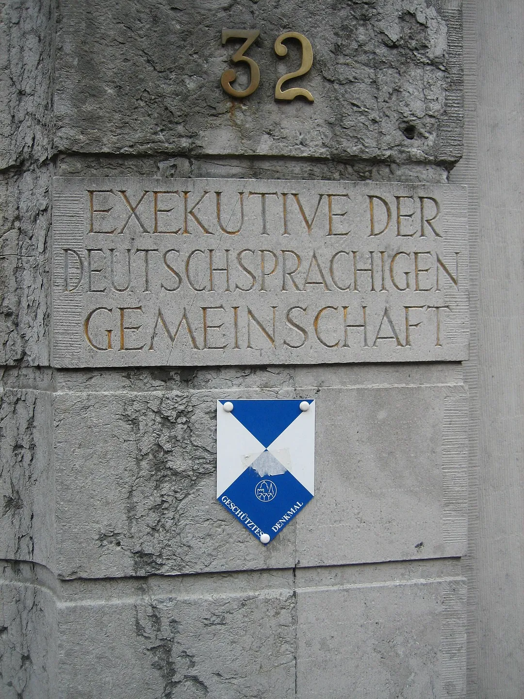 This picture was taken on 06/17/05 in front of the Council of the German Speaking Community in Belgium, which is located in the city of Eupen. The words "Exekutive der deutschsprachigen Gemeinschaft" ("Council of the German Speaking Community") are etched into the pillar, which lines the metal gate leading to the courtyard of the two-story council. Beneath the inscription is a plackard which reads "Geschütztes Denkmal" ("monumental protection"). Structures bearing this seal may not be destroyed or modified without permission, as they may be of historical value.