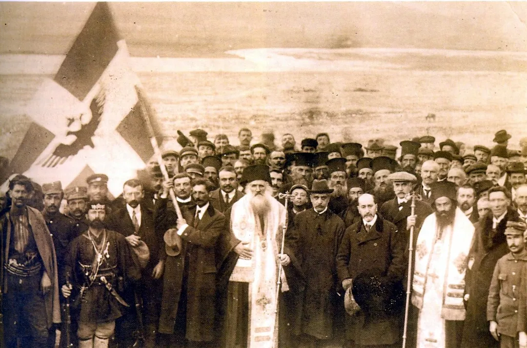 Picture of the illegal declaration of Independence Argirocastro (Gjirokastër) on 1 March 1914. President Georgios Christakis and members of the provisional Government of so called "Northern Epirus", bishops Vasili/Vasileios and Spiridhoni/Spyridon as well as local orthodox clergy, military personnel and civilians pose together with the automony flag. Drini river in the backround.