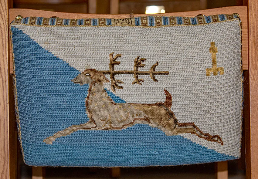 Guildford cathedral kneeler featuring the stag symbol of Stag Hill, the cathedral's location, and a representation of the guilded statue on top of the tower.