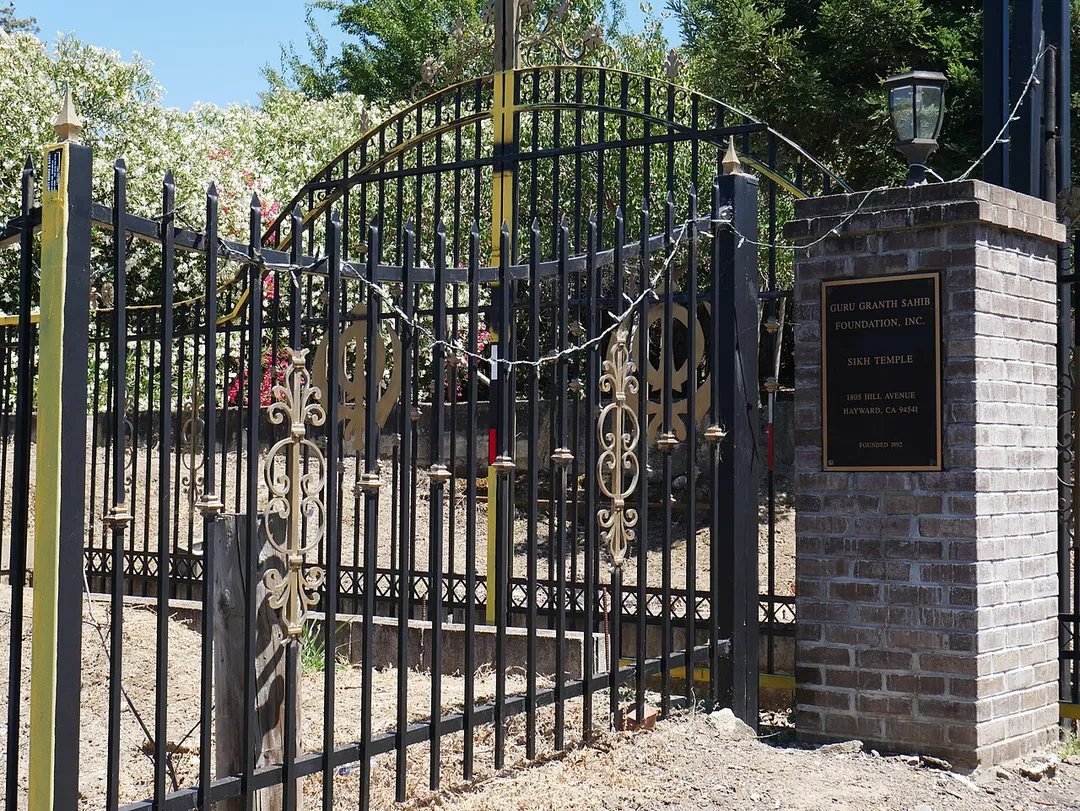 Side gate of Gurdwara Sahib in Hayward, California, with Sikh symbols and dedication plaque.