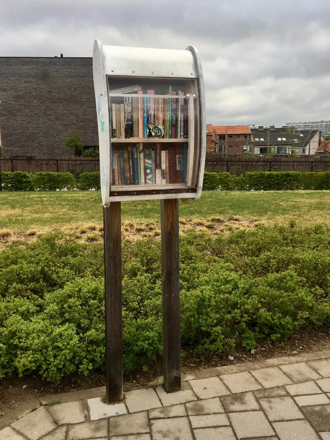 Typical public bookcase on an overcast day where people can freely take or leave books for others in Heverlee, near Leuven, Belgium. Part of the skyline of Heverlee can be seen in the background.