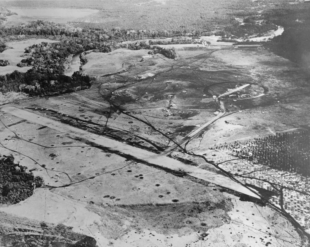 Henderson Field, Guadalcanal, photographed from a USS Saratoga (CV-3) plane in the latter part of August 1942, after U.S. aircraft had begun to use the airfield. The view looks about northwest, with the Lunga River running across the upper portion of the image. Iron Bottom Sound is just out of view at the top. Several planes are parked to the left, and numerous bomb and shell craters are visible.