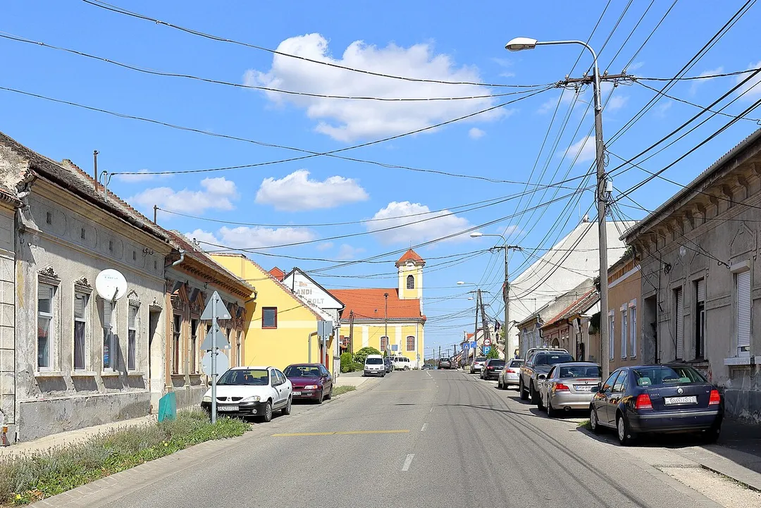 Blick von der Szabadság Utca Richtung Ost in der westungarischen Kleinstadt Jánossomorja. In der Bildmitte die katholische Kirche St. Johannes, die die Erzherzogin Maria Christine Habsburg und ihr Gatte Albert-Casimir Kurfürst von Sachsen-Teschen im Jahr 1769 erbauen ließen.