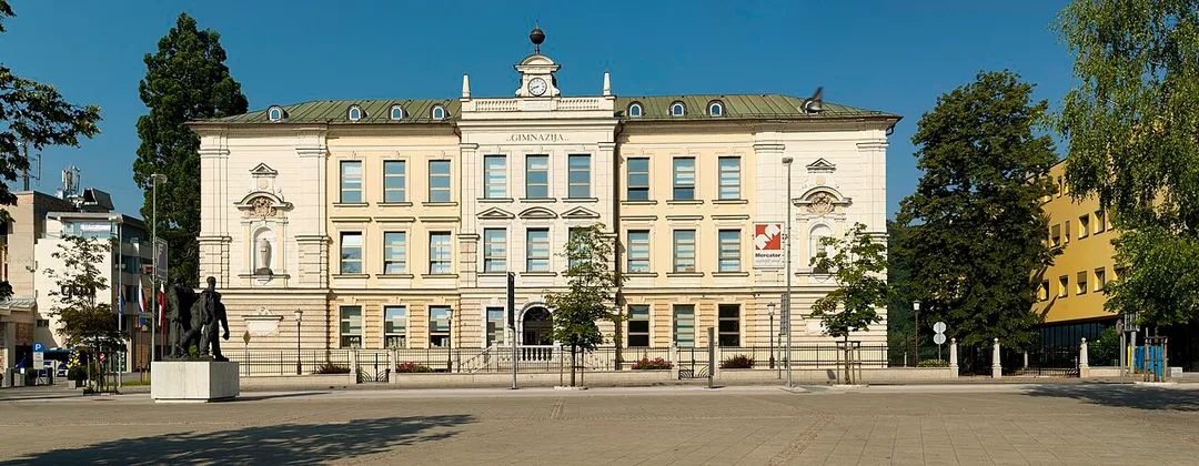Kranj Gymnasium, next to Slovene Square (Slovenski trg). The historicist building was completed in 1897 according to plans by Viljem Treo (1845–1926) from Ljubljana. The sculpture in the front is work by Lojze Dolinar (1893–1970).