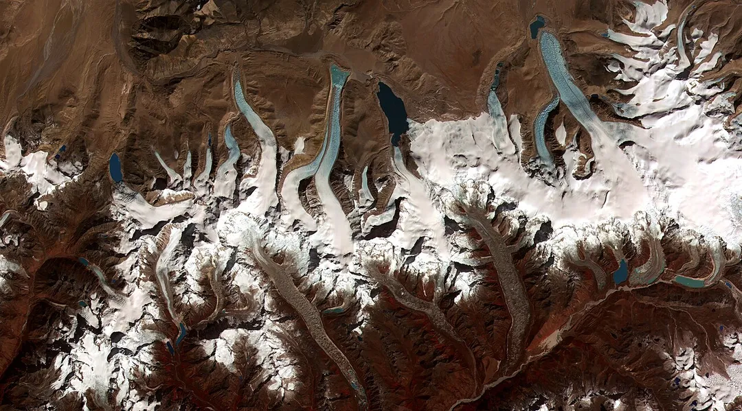 This image shows the termini of the glaciers in the Bhutan-Himalaya. Glacial lakes have been rapidly forming on the surface of the debris-covered glaciers in this region during the last few decades. USGS researchers have found a strong correlation between increasing temperatures and glacial retreat in this region.
According to a joint press release issued by NASA and the U.S. Geological Survey, the great majority of the world’s glaciers appear to be declining at rates equal to or greater than long-established trends. This image from the ASTER (Advanced Spaceborne Thermal Emission and Reflection Radiometer) instrument aboard NASA’s Terra satellite shows the termini of the glaciers in the Bhutan-Himalaya. Glacial lakes have been rapidly forming on the surface of the debris-covered glaciers in this region during the last few decades.

According to Jeffrey Kargel, a USGS scientist, glaciers in the Himalaya are wasting at alarming and accelerating rates, as indicated by comparisons of satellite and historic data, and as shown by the widespread, rapid growth of lakes on the glacier surfaces. According to a 2001 report by the Intergovernmental Panel on Climate Change, scientists estimate that surface temperatures could rise by 1.4°C to 5.8°C by the end of the century. The researchers have found a strong correlation between increasing temperatures and glacier retreat.
