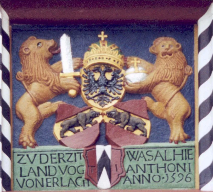 The stack of crests above the main gate of castle Lenzburg: at the bottom, the coat of arms of the von Erlach family, above that the flag of the canton of Bern, all topped by the Reichsadler of the Holy Roman Empire.