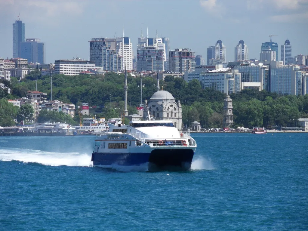 Catamaran ferry made by Austal for İDO in 1996 (length: 40 meters, top speed: 34 knots, capacity: 450 people), at the Bosphorus strait in Istanbul, Turkey. The Dolmabahçe Mosque and Dolmabahçe Clock Tower can be seen near the coastline, while the skyscrapers of Levent business district are seen further behind.