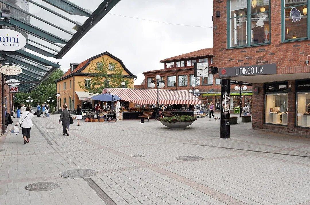 Torget vid Lidingö centrum. Det gula huset i bakgrunden inrymde innan Lidingö centrum byggdes, bland annat Lidingö Järnaffär och i övre planet bostäder. Idag inrymmer huset bland annat en restaurang och en pub. Nya Lidingö Järnaffär valde att förlägga sin verksamhet vid Kyrkviken invid de gamla spårvägshallarna som idag är ett hotell.