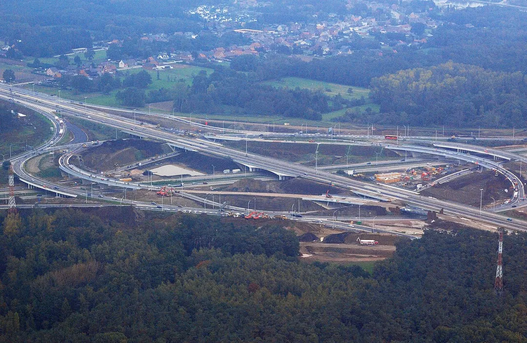 Aerial photograph of the motorway intersection near Lummen, Belgium, viewed from the southwest, during major refurbishment works. The village in the background is Genenbos, part of the municipality of Lummen. In the upper right corner the Albert Canal can be distinguished. Nikon D60 f=55mm f/9 at 1/320s ISO 800. Contrast and colours enhanced using Nikon NX Studio 1.3.2. Framed using GIMP 2.10.34.