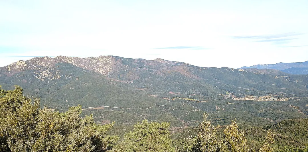 Maçanet de Cabrenys is a municipality in the "comarca" of Alt Empordà.
Roc de Frausa (1450 metres altitude) is the highest point on the ridge above the village, to the left. The exposures along and below that ridge are of Ordovician orthogneiss.
The view is from the south-west, from a hilltop by the Santa Maria de la Fau church.