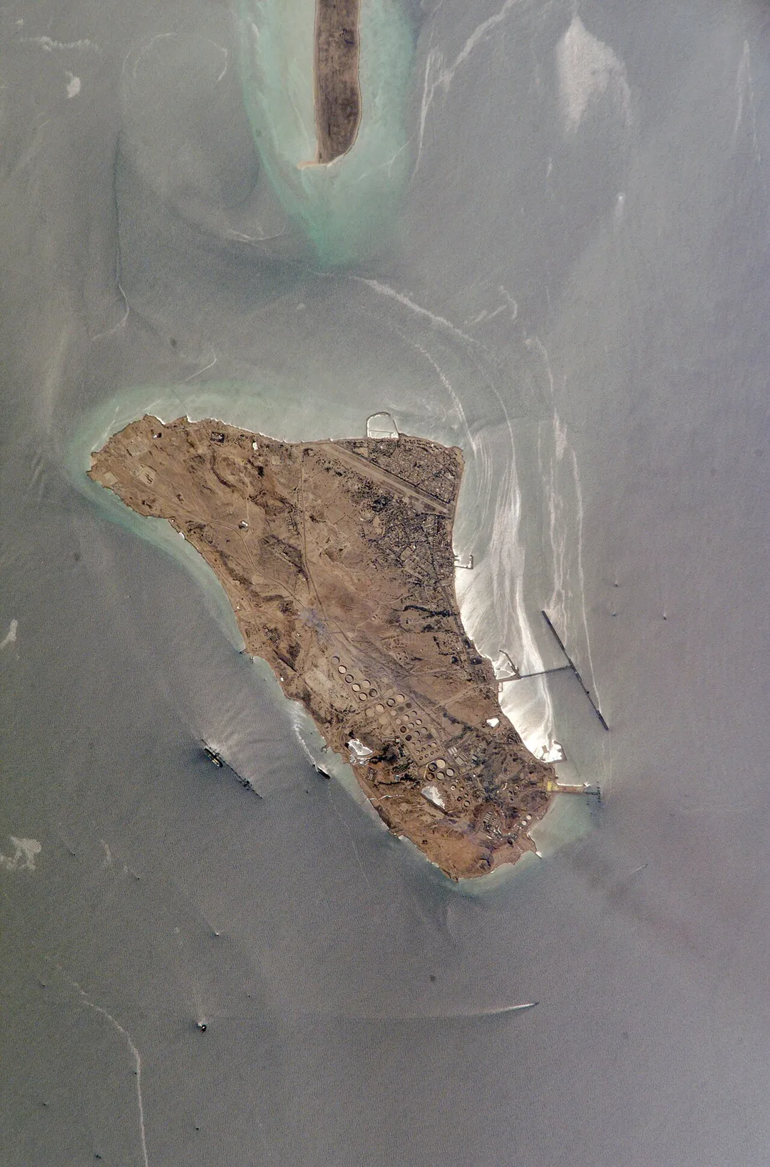 Kharg Island is Iran’s primary oil export terminal in the Persian Gulf. This rocky limestone island is unique because it is one of the few islands in the Persian Gulf with freshwater which has collected within the porous limestone. In addition to its commercial and strategic importance, the freshwater has biological importance, supporting populations of gazelles. This high-resolution photograph taken by astronauts on board the International Space Station shows detail of the tanker dock facilities, tanks and other infrastructure. Sunglint on the surface of the water highlights small amounts of oil on the sea surface and reveals the direction of the local currents.