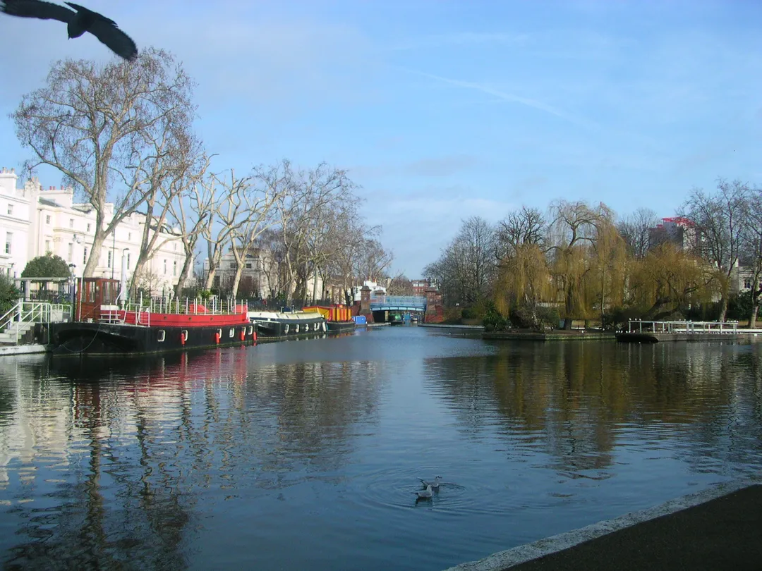 Little Venice basin viewed from the western end looking north-east towards the Regents Canal corner, with the island on the right and white Regency style terraces overlooking the basin.