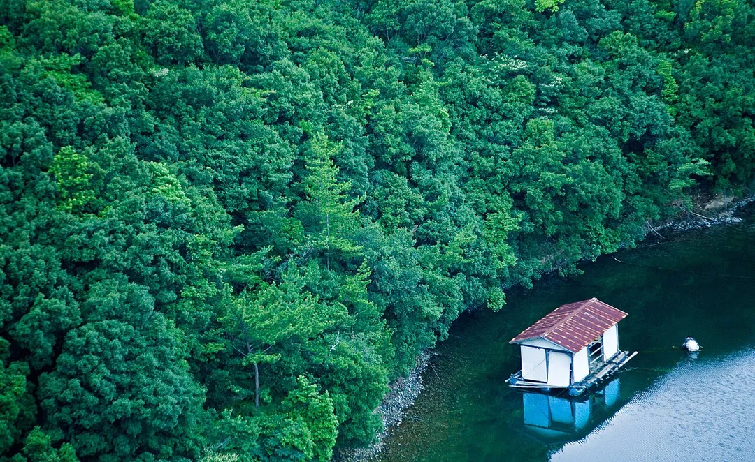 A boat house resting peacefully by the riverside trees

Needs additional description