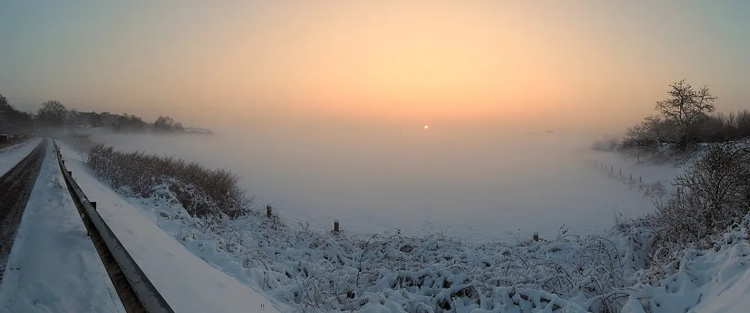 Panoramic view over the Felder (name of this area of the local inhabitants) in the Moers district Schwafheim, North Rhine-Westphalia, Germany, immersed in a deep fog during the sunset on a slightly overcast winter day in December. View from Düsseldorfer Straße. Part of this can be seen on the left side.