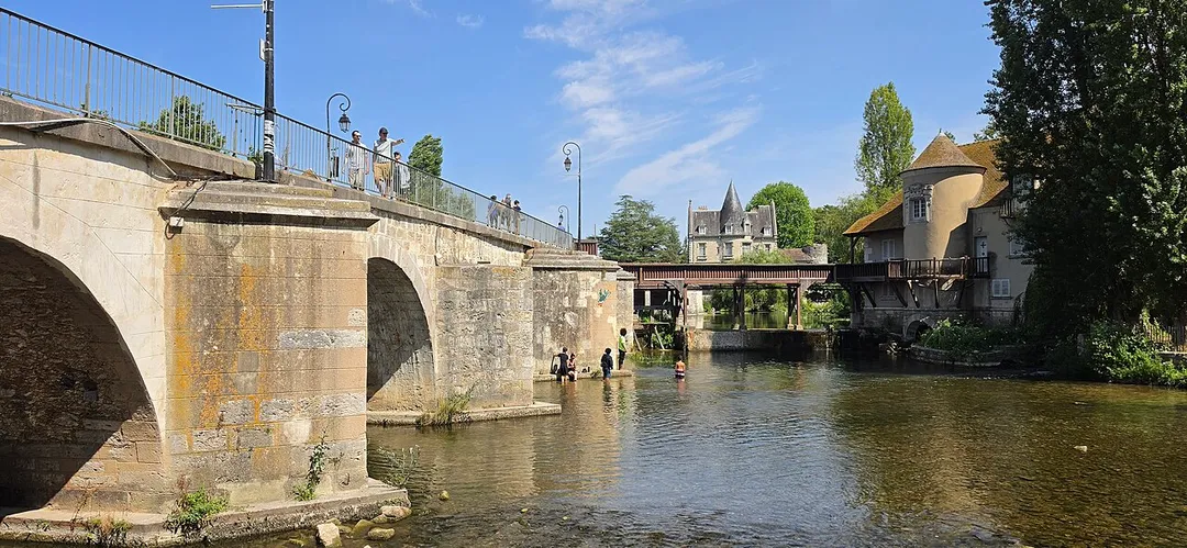 The 12th-century bridge crossing the Loing River, a site frequently depicted in Impressionist paintings.In the background, the Old Mill of Moret (Le Moulin de Moret) can be seen resting on wooden supports above the water.