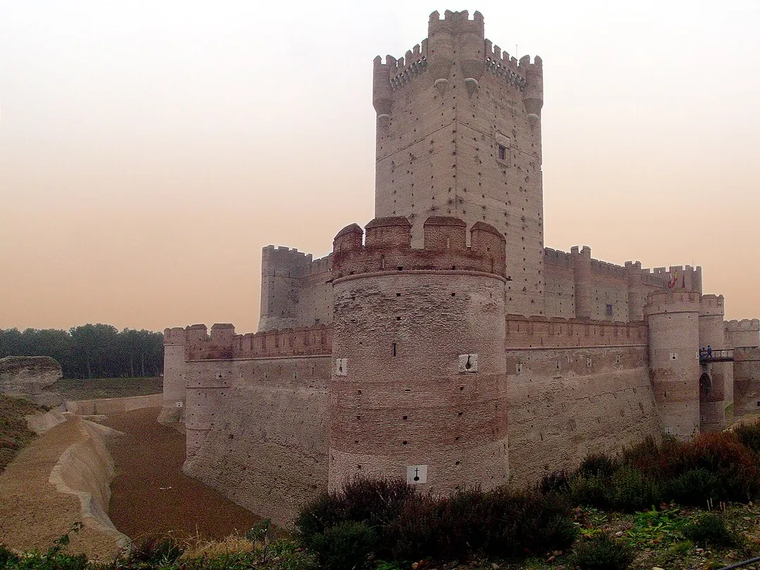 The Mota Castle in Medina del Campo (Valladolid, Spain). The word “Mota” refers to an artificial mountain built to defend the castle better, this mound was called in early English: motte. The Mota fortress had a military function and it also was a royal dungeon. The castle was built between the 12th and 15th Centuries. It has a coat with its own drawbridge (today fixed), an outer curtain (for artillery), an inner curtain (with arrow slits for archers and guards) surrounding a large courtyard, and a great square tower (which is the Keep).The castle was left and collapsed, but was recovered after the Spanish Civil War (1936-1939). It is the first monumental building in Medina declared Good with Cultural Interest.