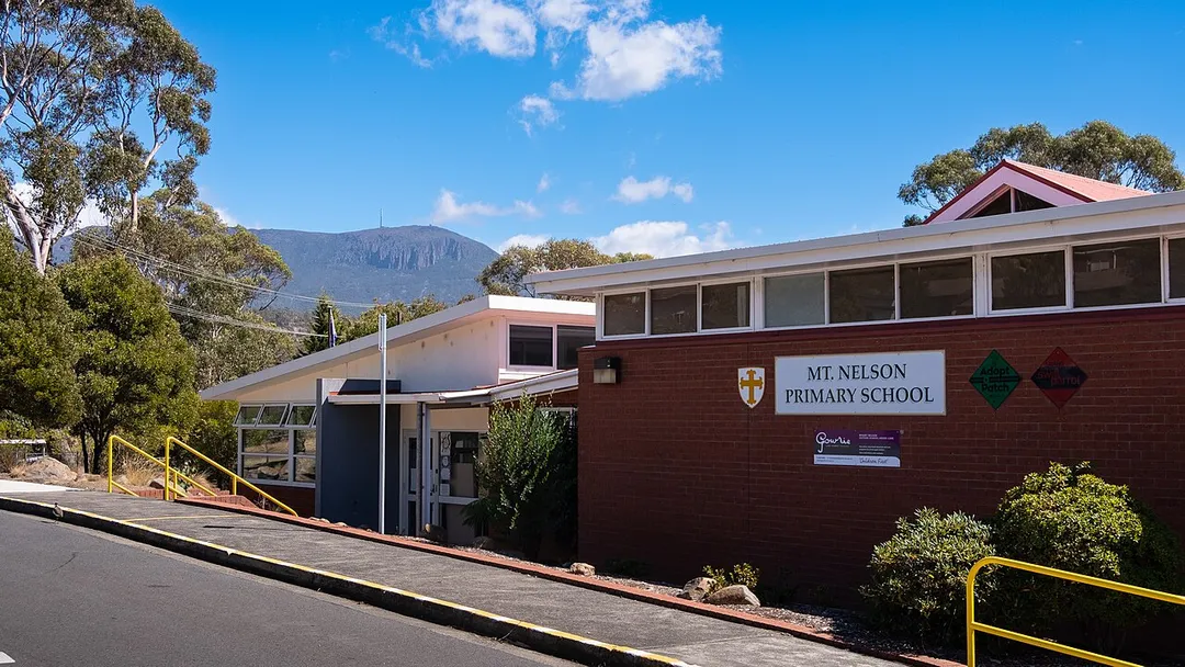 The image showcases Mount Nelson Primary School, a vibrant hub of learning nestled amidst lush greenery. Tall trees provide shade, adding to the serene atmosphere of the school grounds. The scene reflects an environment conducive to education and growth backdropped by kunanyi/Mount Wellington.
