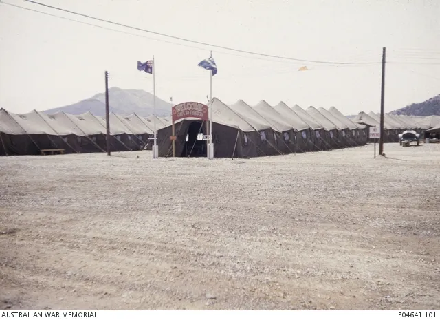 " Welcome Gate to Freedom" at Freedom Village, Munsan-ni. The Australian flag and possibly the flag of the 28th Commonwealth Brigade fly above the gate at the head of a long tent used to receive Australian prisoners of war (POWs) released by the North Korean and Chinese during Operation Little Switch and again later during Operation Big Switch. One of a series of photographs taken by the Australian Mr Douglas (Doug) Bushby in his capacity as a UN accredited War Correspondent. Mr Bushby devoted much of his time to relief and missionary work amongst Korean refugees, orphans and North Korean and Chinese prisoners of war.