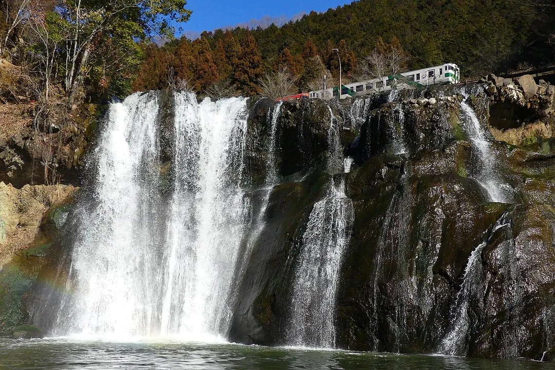 A panoramic view of Ryumon Falls in Nasukarasuyama City, Tochigi Prefecture. A Kiha 40 series diesel train on the JR Karasuyama Line is running in the back.